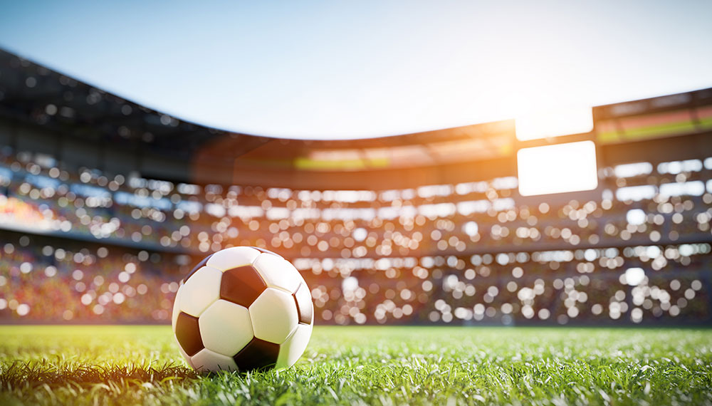 Soccer ball on pitch with stadium in background